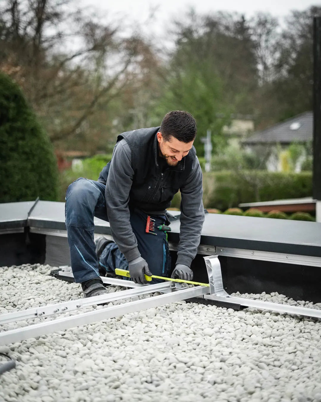 Monteur misst die Unterkonstruktion für eine Solaranlage auf einem Kiesdach aus