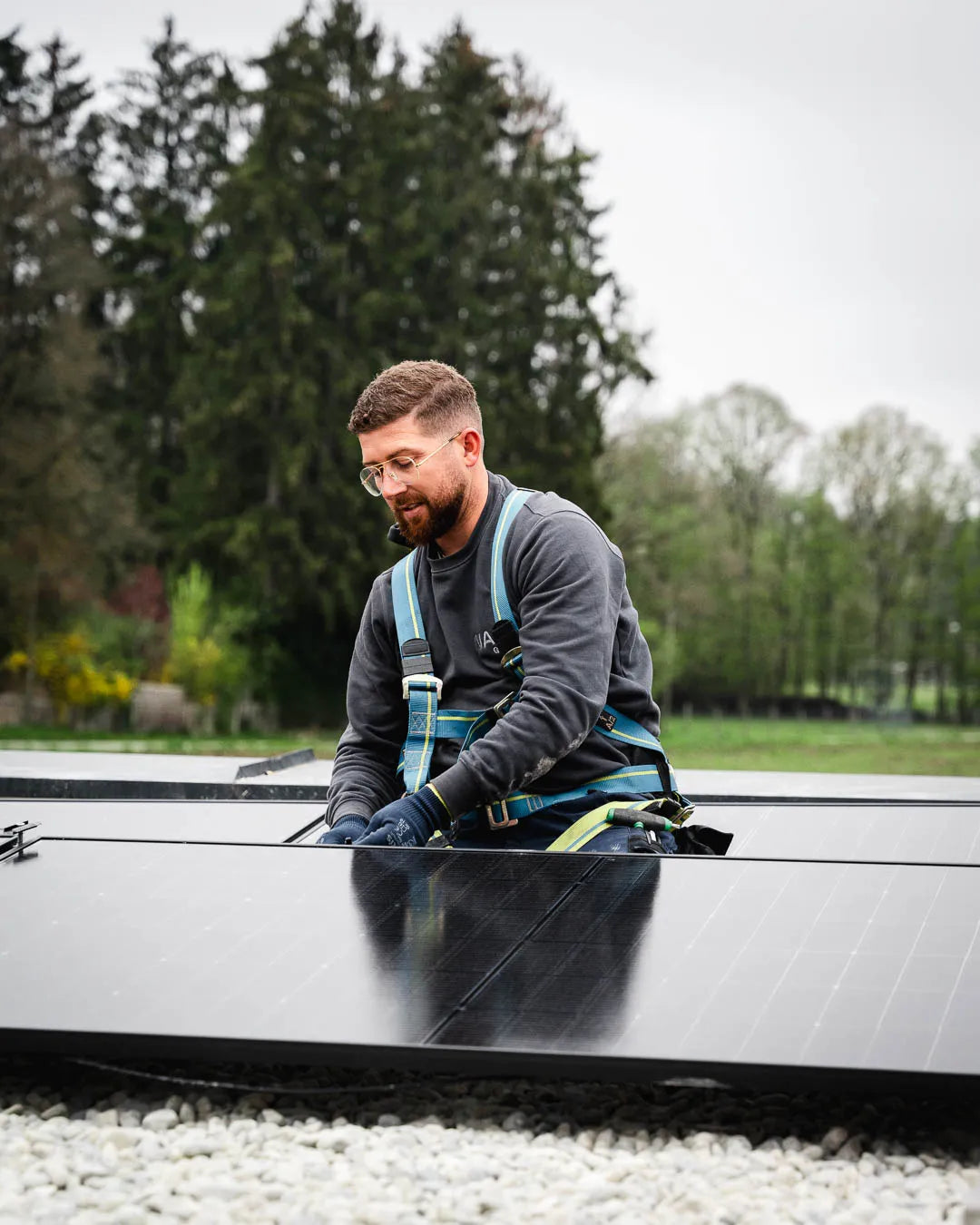 Monteur mit Sicherungsgurt richtet ein Solarmodul auf dem Flachdach aus